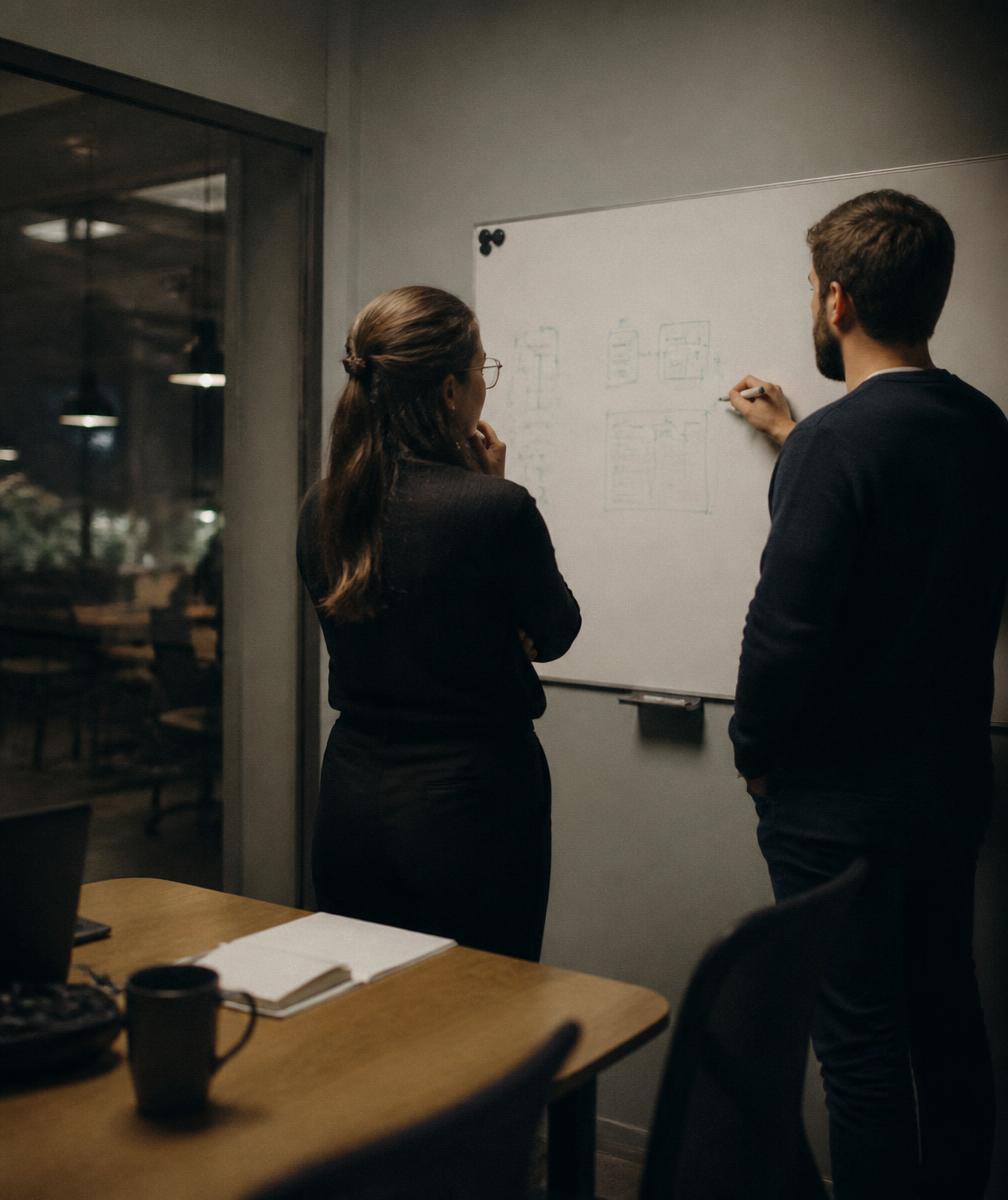 Two colleagues reviewing a diagram on a whiteboard in a small meeting room
